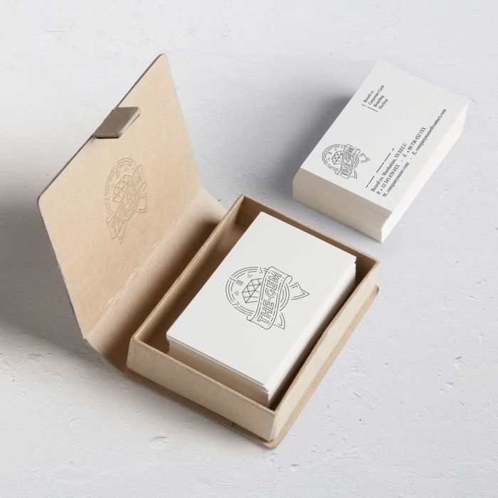 A stack of white business cards with a simple logo and text is shown; some cards are in a brown cardboard box while others are stacked outside on a white surface.