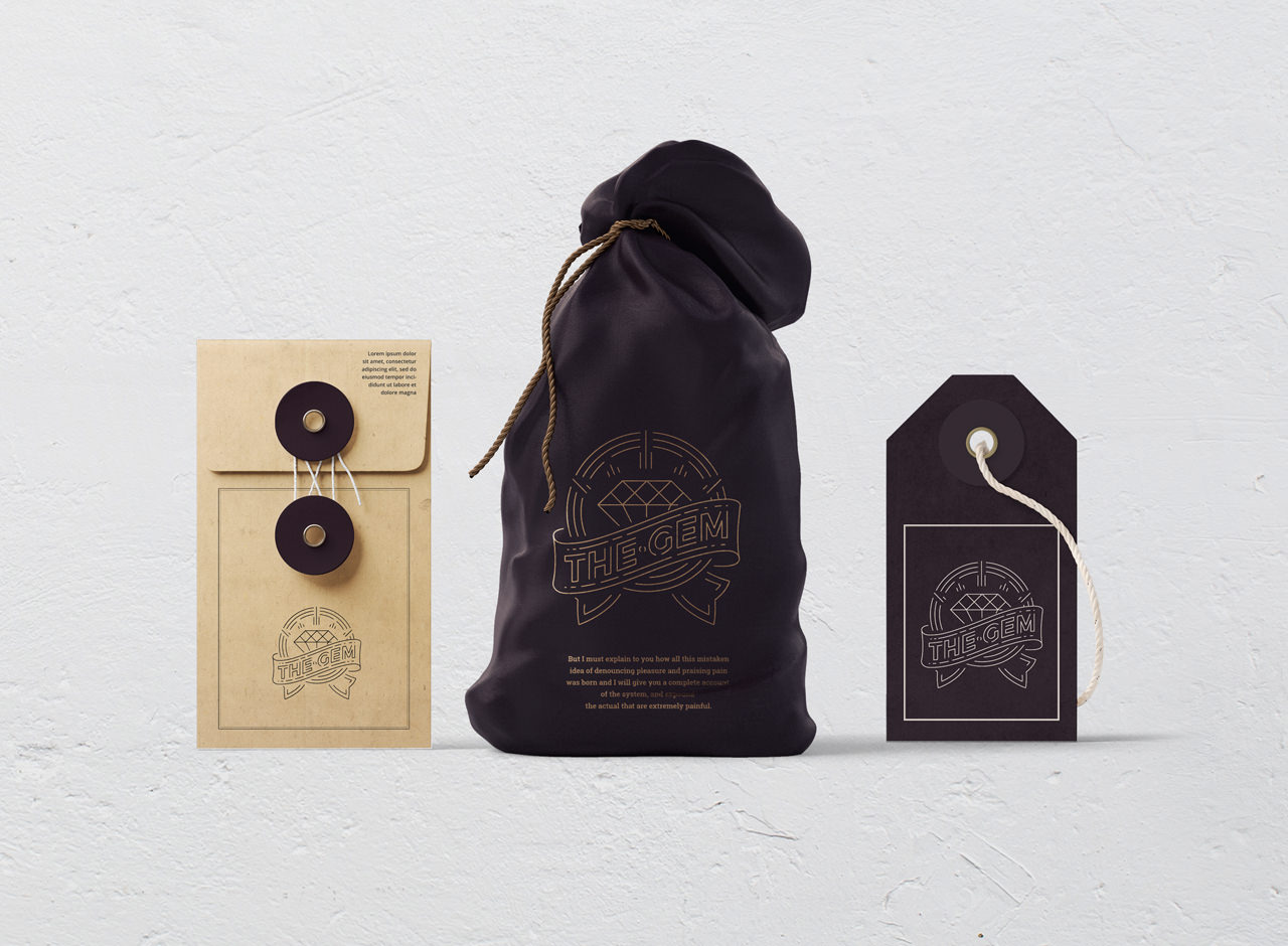 Three items with The Gem logo: a tan envelope with a string closure, a dark drawstring pouch, and a dark tag with a white string, all arranged against a plain white background.