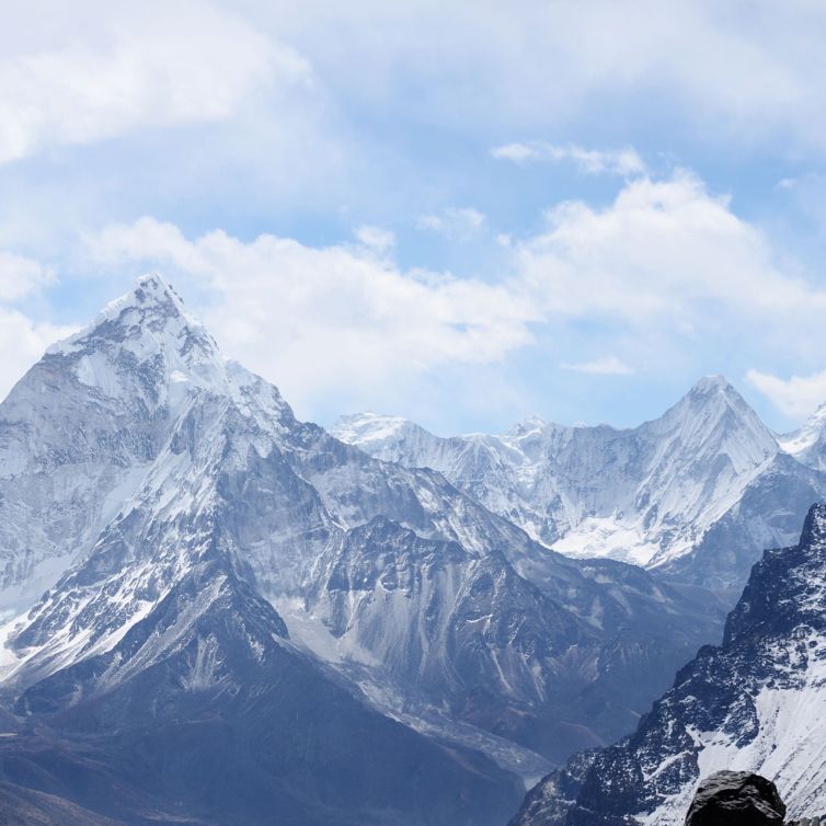 Snow-capped mountains under a partly cloudy sky, with rugged peaks and ridges extending into the distance. The scene is serene and majestic, showcasing the natural beauty of a high-altitude mountain range.