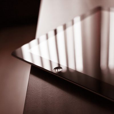 A close-up of a tablet lying on a table, with light and shadows from window blinds reflecting on its screen. The home button is visible in the foreground.