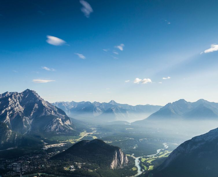 A panoramic view of a lush green valley surrounded by rugged mountain ranges under a clear blue sky, with a winding river running through the landscape.