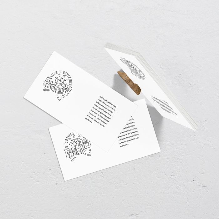 Three white business cards with black text and a circular logo are arranged on a textured white surface. Two cards are flat, showing the logo and text, while one is propped up at an angle with a small wooden stick.