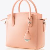 A small, structured handbag in light peach leather with two top handles, subtle texture, silver hardware, and a decorative leather tag hanging from one handle. The bag is set against a plain white background.