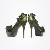 A pair of high-heeled shoes painted metallic green with decorative green ribbon accents on the front and sides, displayed on a white background with the heels facing forward.
