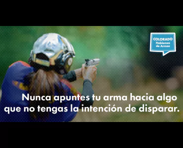 A person wearing earmuffs aims a handgun at a shooting range with the Spanish text: Nunca apuntes tu arma hacia algo que no tengas la intención de disparar and a Colorado Hablemos de Armas logo.